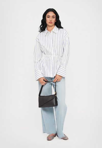 Camicia a maniche lunghe bianca e blu a righe, legata in vita, abbinata a jeans azzurri chiari e a una borsa a tracolla nera. Scarpe a righe multicolori.