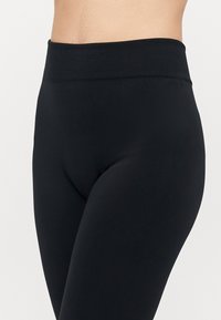Schwarze Leggings mit einem breiten, elastischen Bund, glatter Textur, figurbetontem Design und einer schlanken Silhouette. Keine sichtbaren Muster.