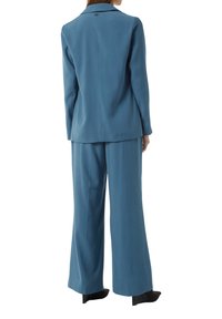 Dwuczęściowy garnitur z teksturowanej tkaniny w kolorze teal; marynarka z klapami i detalem w postaci guzików, spodnie z szerokimi nogawkami o luźnym kroju.