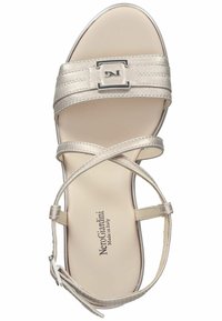 Sandale beige avec une finition brillante, présentant des brides croisées, un accent de boucle carrée et une bride de cheville confortable. Semelle plate avec marquage.