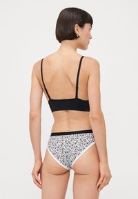 Melna bralette ar plānām siksniņām, kas apvienota ar baltām apakšbiksēm ar ziedu rakstu. Gluda auduma ar kontrastējošu melnu jostu.