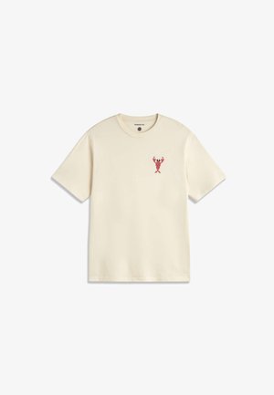 T-shirt à manches courtes blanc cassé avec un petit graphisme de homard rouge sur le côté gauche de la poitrine et une étiquette "Thinking Mu" à l'intérieur du col.