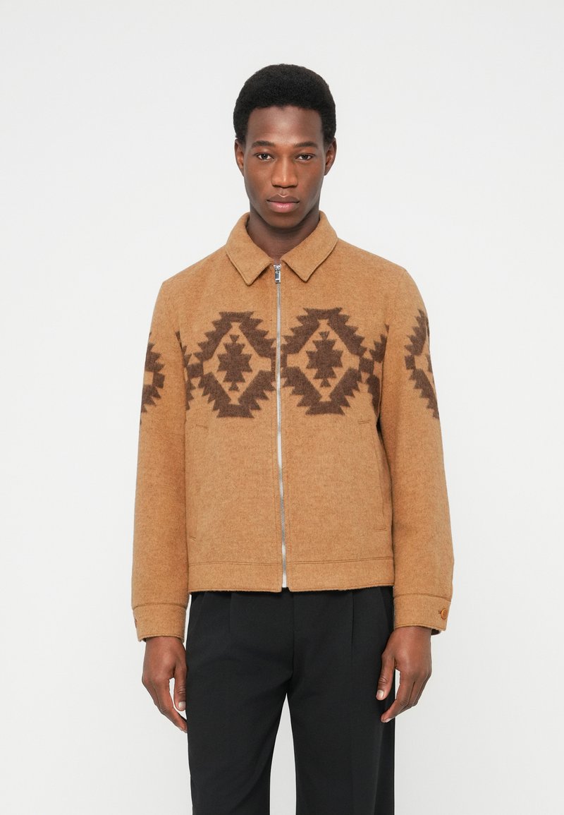 Brun uldjakke med geometriske mønstre i mørkebrun. Har krave og lynlås foran. Tekstureret stof og skræddersyet pasform.