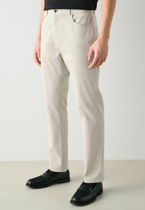 Chinos beige avec une coupe slim, poches latérales et une fermeture éclair. Associés à des mocassins noirs avec une tige texturée. Fini en tissu lisse.