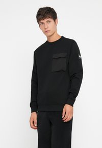 Black sweatshirt with a crew neckline, featuring a front pocket and branding on the sleeve. Made of soft material with a smooth texture.