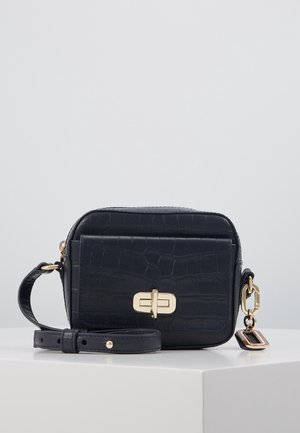 Kleine zwarte crossbodytas met krokodillenstructuur, draaiknopsluiting in goudkleur, verstelbare band en decoratieve gouden en zwarte bedel.