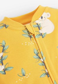 Gul lynlåsbeklædning med et koala- og bladmønster, blød tekstur og ribbet halsudskæring. Designet inkluderer små hvide detaljeringer.