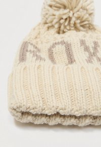 Pletená čiapka v krémovej farbe s rebrovaným lemom a pom-pom vrcholom. Má svetlohnedé dekoračné vzory po celom povrchu.