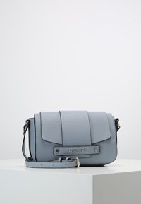 Ljusblå läder crossbody-väska med en vikbar klaff, silverdetaljer och ett avtagbart rem. Har präglad logotyp på framsidan.