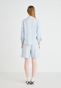 Completo in lino azzurro chiaro con camicia colletto a maniche puff e pantaloni corti abbinati. Design semplice con vestibilità comoda.