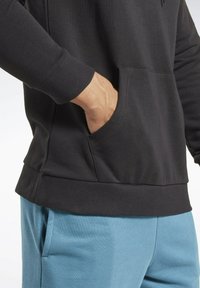 Sudadera negra con puños acanalados y un bolsillo delantero, combinada con pantalones de chándal azul claros, mostrando una textura de tela suave.