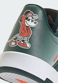 Zelené kožené tenisky s obrázkom rozprávkového charakteru, červenými akcentmi a textúrovanou bielou podrážkou. Výrazné grafiky na boku.
