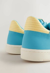 Sneakers blu con una texture liscia e collare imbottito giallo. Presentano suole in gomma bianca e sottili dettagli di cucitura.
