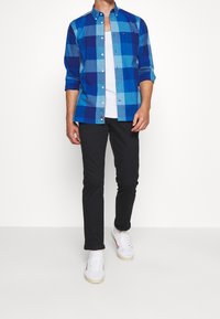 Blå rutig skjorta med lång ärm, knappad krage och bröstficka, kombinerad med svarta byxor och vita sneakers.