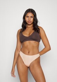 Barna melltartó mély V-kivágással és vékony pántokkal, amelyet testszínű, magas derekú bikini alsóval párosítottak, sima textúrával és egyszerű dizájnnal.