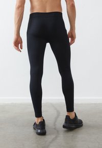 Črne športne legice iz raztegljivega materiala, z visokim pasom in gladko teksturo. Nosi se z črnimi športnimi čevlji.