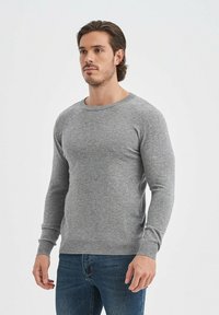 Pull en maille gris à manches longues, col rond et poignets côtelés. Associé à un jean bleu foncé pour un look décontracté.