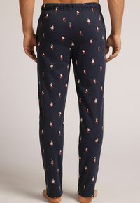 Pantalones de pijama de un azul marino oscuro con una cintura elástica, que presentan un patrón repetido de pequeños personajes de dibujos animados coloridos sobre una tela suave.