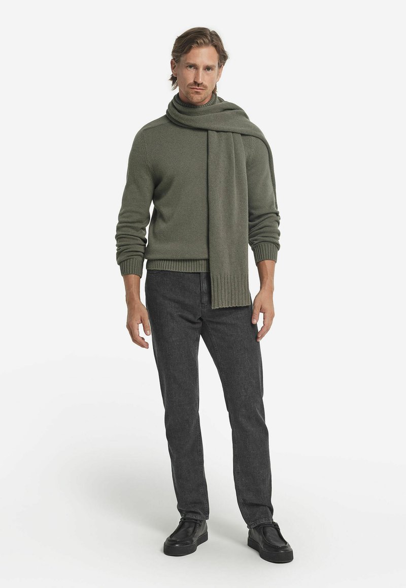 Oliven grøn strikket trøje med et matchende tørklæde, parret med mørkegrå jeans og sorte sko. Alle genstande har et simpelt, klassisk design.