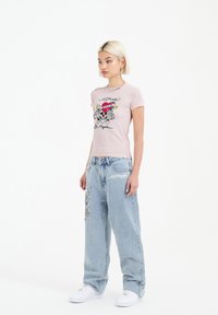 Pink short-sleeve t-shirt with skull and script print, paired with light blue baggy jeans featuring colorful embroidered designs.
