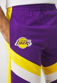 Pantalones cortos morados con rayas amarillas y blancas, con el logo de Los Angeles Lakers. Hechos de tela suave con una cinturilla elástica.