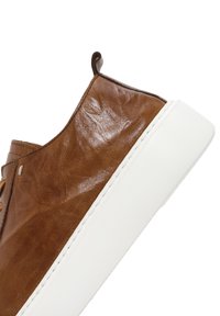 Basket en cuir marron avec une finition texturée, dotée d'une semelle en caoutchouc blanche et d'un design minimaliste. Comprend une petite sangle à l'arrière.