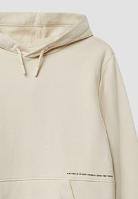 Cremfarbener Hoodie mit Kordelzugkapuze, Fronttasche und bedrucktem Text "NATURE IS IN OUR HANDS | SAVE THE TREES" am Saum. Glatte Textur.