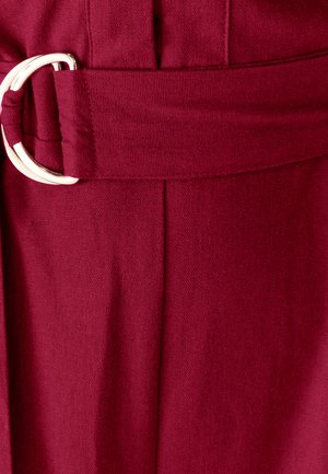 Zbliżenie na burgundowy pasek materiałowy z metalowym zapięciem w kształcie litery D na odzieży.