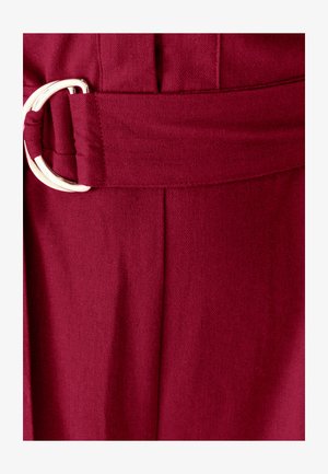 Zbliżenie na burgundowy pasek materiałowy z metalowym zapięciem w kształcie litery D na odzieży.