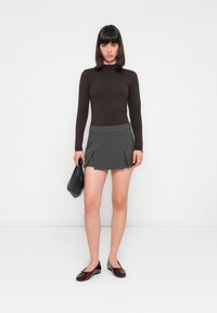 Top bej cu mâneci lungi, fustă mini plisată gri, geantă neagră și pantofi balerini din piele lăcuită burgundy. Concentrează-te pe linii curate și o siluetă ajustată.