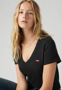 Camiseta negra de manga corta y cuello en V, hecha de algodón suave, con una pequeña etiqueta del logo rojo de Levi's en el lado izquierdo, cerca del pecho.