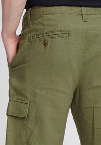 Pantalons cargo vert olive en tissu texturé, dotés d'une poche arrière avec fermeture à bouton et d'une poche latérale pour un rangement supplémentaire.
