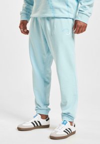 Light blue sweatpants with elastic cuffs, featuring a subtle logo and a relaxed fit, paired with white and black sneakers.