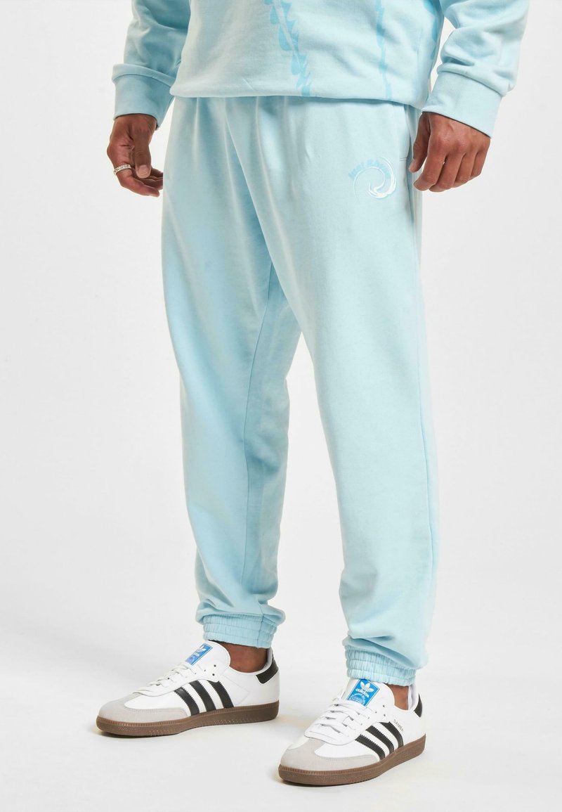 Light blue sweatpants with elastic cuffs, featuring a subtle logo and a relaxed fit, paired with white and black sneakers.
