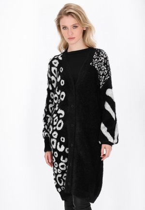 Cardigan lungo, nero e peloso, con stampa leopardata bianca e motivi a strisce; presenta una scollatura a V, maniche lunghe e chiusura con bottoni.