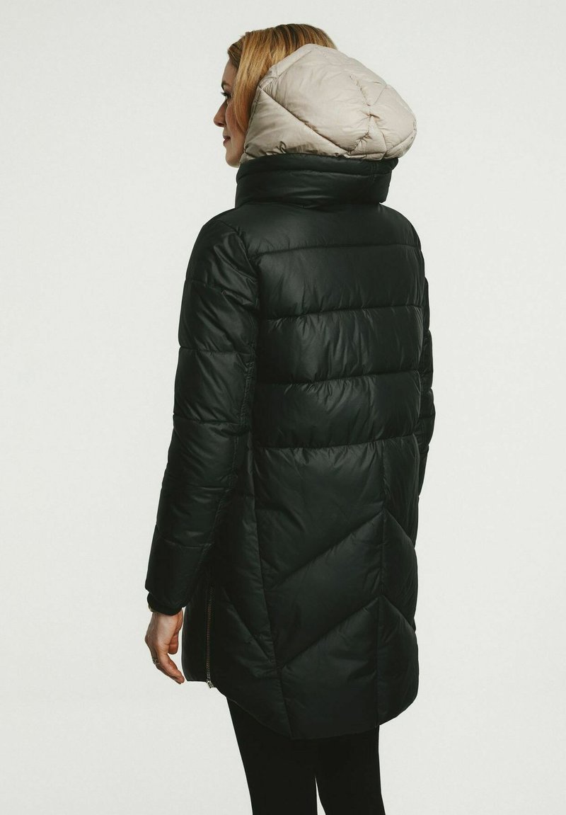 Schwarze Pufferjacke mit einer beigen Kapuze, die ein gestepptes Muster, einen hohen Kragen und seitliche Reißverschlusstaschen aufweist. Die Rückansicht zeigt ein verlängertes Design.