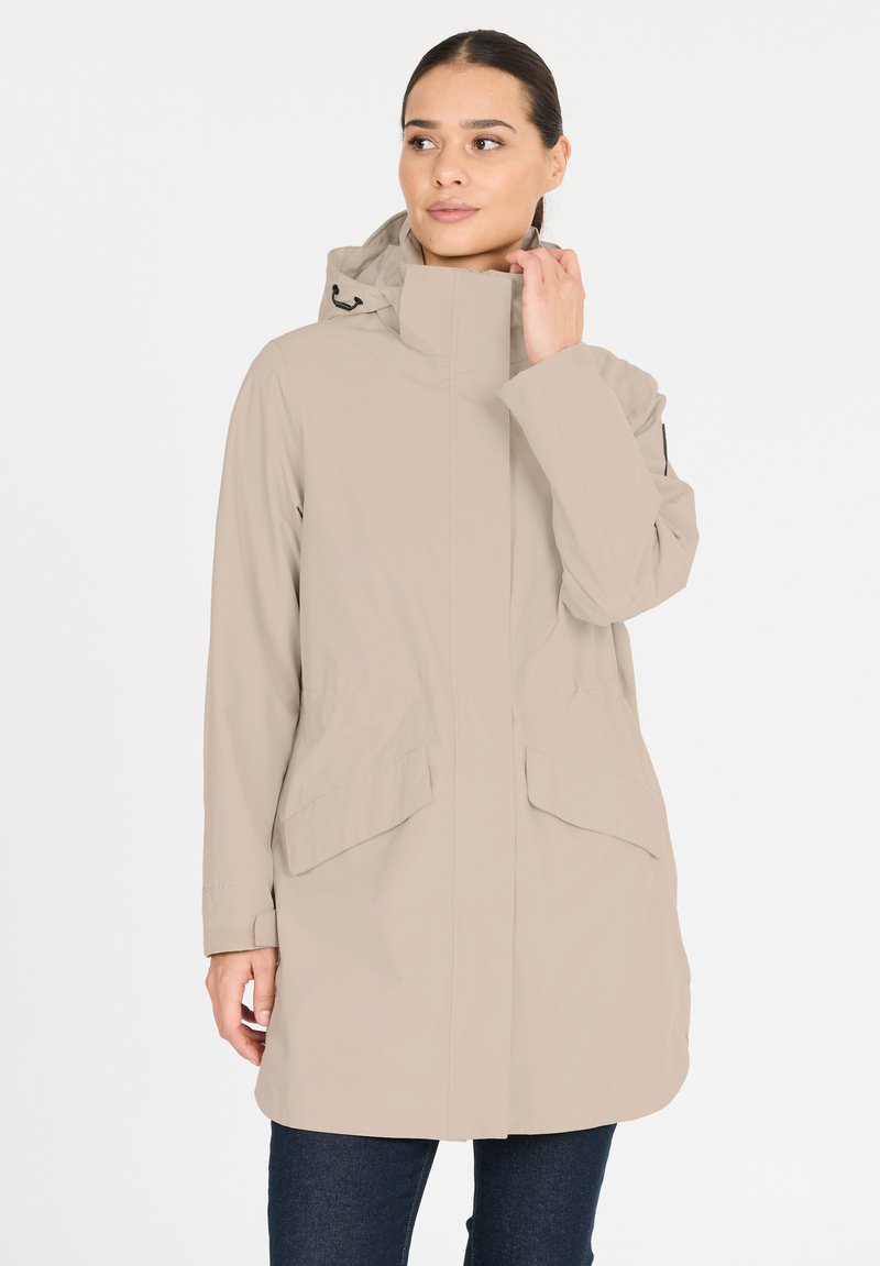 Veste imperméable beige avec capuche, deux poches avant, poignets et un design épuré. Texture lisse et matériau léger.