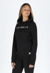 Black hoodie made of soft fabric featuring a kangaroo pocket, drawstring hood, and "LOS ANGELES" printed in white on the front.