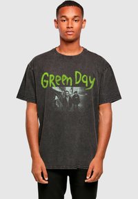 Camiseta negra de gran tamaño con un aspecto desgastado, que presenta el texto verde "Green Day" y una imagen en blanco y negro de la banda en el frontal.