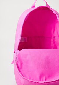 Roze stoffen rugzak met een hoofdcompartiment, een gladde textuur, een eenvoudig ontwerp en een zichtbaar etiket aan de binnenkant. Geen extra vakken aanwezig.
