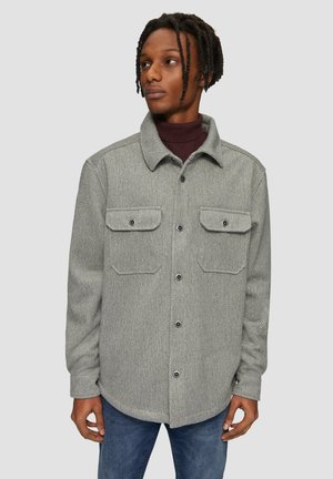 Grijs herringbone overhemdjasje met twee borstzakken, knoopsluiting en een kraag. Draag het over een bordeauxrode coltrui. Casual pasvorm ontwerp.