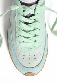 Zapatillas verde menta con materiales de malla y ante, cordones planos, caja de puntera perforada y suela de goma. Presenta acentos morados en la lengüeta.