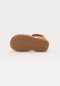 Semelle de sandale en caoutchouc tan avec des motifs de grip circulaires texturés, sangle réglable et design ouvert pour une bonne respirabilité.