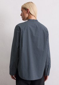 Donkere blauwe blouse met lange mouwen en een geometrisch patroon. Voorzien van een mandarincol en een ontspannen pasvorm, met knoopmanchetten.
