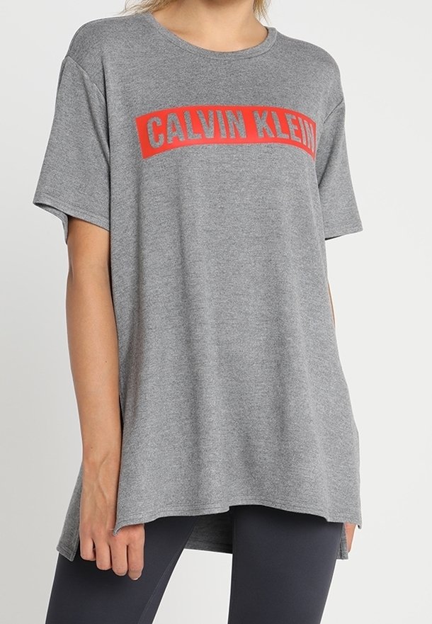 Szara bawełniana koszulka z krótkim rękawem i okrągłym dekoltem, z wyraźnym czerwonym nadrukiem logo "CALVIN KLEIN" na klatce piersiowej.
