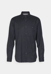 Svart långärmad skjorta med knappar och spetsig krage, samt liten broderad logotyp på bröstet mot en neutral bakgrund.