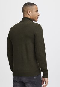 Pulover tricotat, de culoare verde închis, cu guler înalt, având o margine și mansete ribbate, prezentat din spate, cu o textură fină și o formă ajustată.