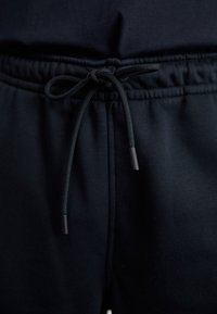 Svarta joggingsbyxor med elastisk midja och dragsko, med en slät textur och minimalistisk design.