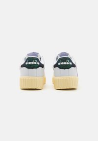 Weiße Sneakers mit einer strukturierten Ferse aus navy- und grünem Mesh, lila Akzenten und einer dicken, cremefarbenen Gummisohle. Logo auf der Rückseite.
