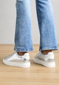 Srebrne trampki wykonane z teksturowanego materiału z białą podeszwą. Ozdobione logo na pięcie i płaskim sznurowaniem.